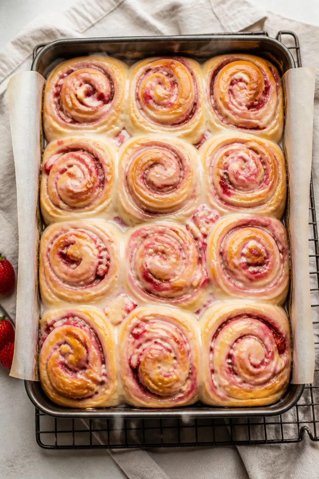 Overhead shot of freshly baked Strawberry Cinnamon Rolls in a 9x13 pan just out of the oven, rolls l