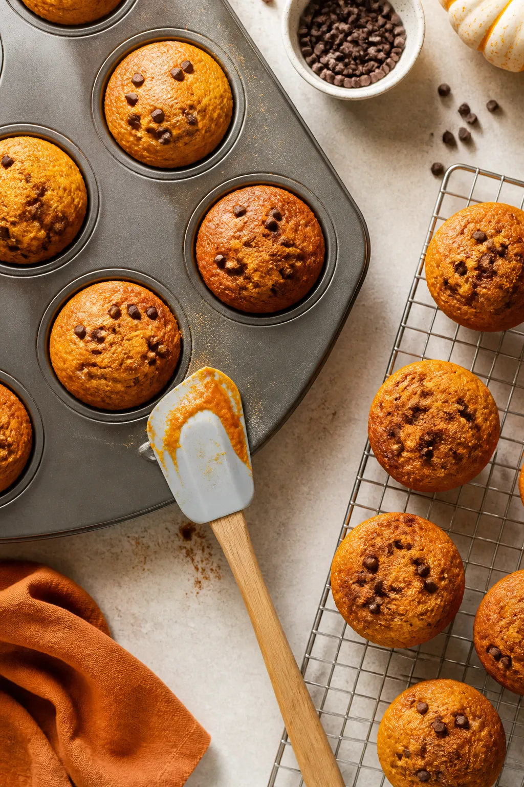 Overhead shot of freshly baked flourless pumpkin muffins cooling in a muffin tin beside a wire rack,